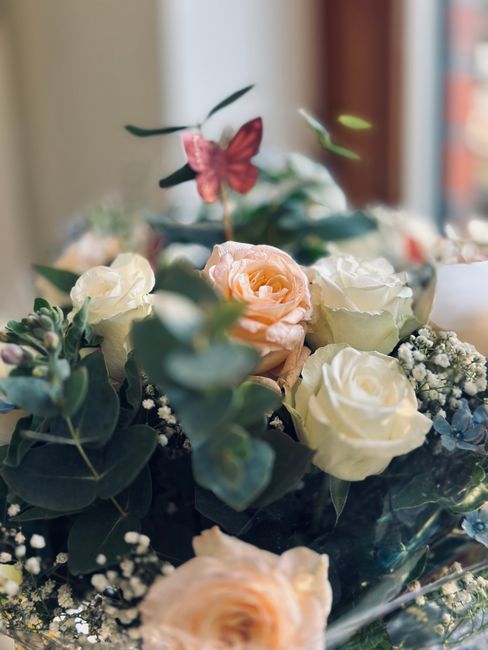A close-up view of a floral gift arrangement featuring cream and light peach roses, interspersed with sprigs of baby's breath. The bouquet is accented with green eucalyptus leaves, and a delicate pink