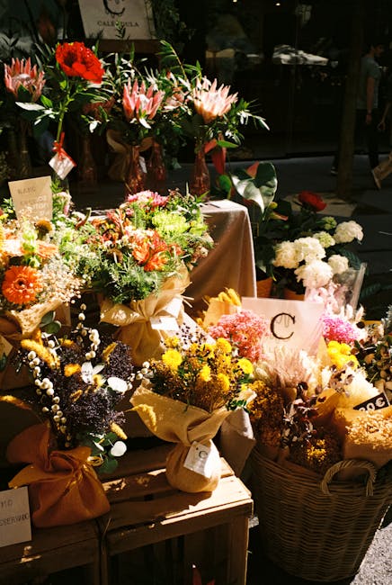 A display of freshly arranged floral bouquets and arrangements at a flower shop, featuring a variety of flowers including pink and white lilies, red gerbera daisies, yellow chrysanthemums, and baby's 