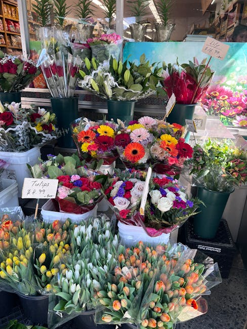 A display of fresh floral arrangements and bouquets at a florist stand, featuring a variety of colourful flowers including orange, yellow, pink, purple, and white blooms. In the foreground, there are 
